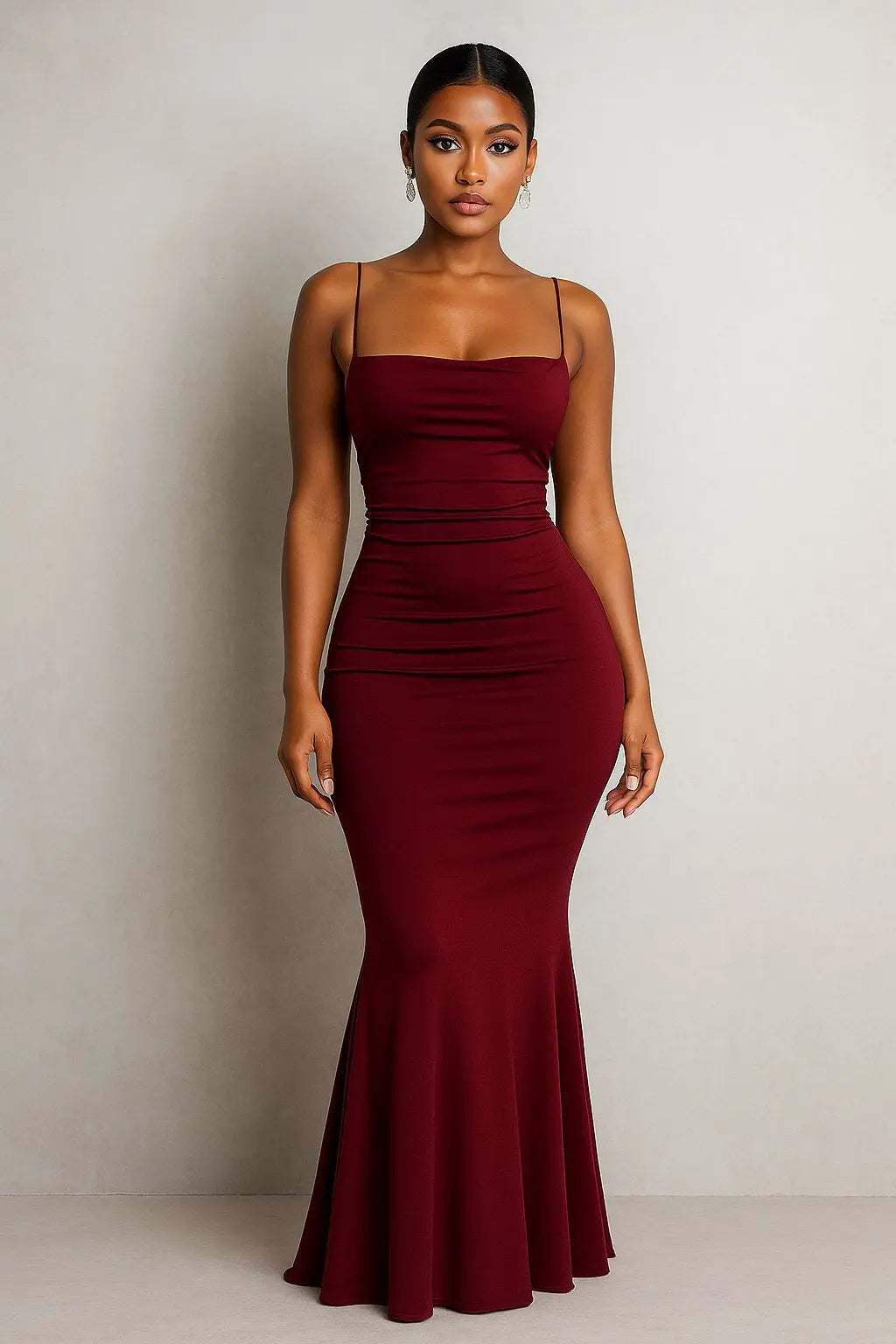 Woman wearing a fitted burgundy Nova Night Out Jumpsuit with thin straps and a flared hem.