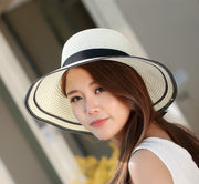 Woman wearing foldable straw sun hat with wide brim and black bow on the beach