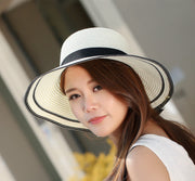 Woman wearing foldable straw sun hat with wide brim and black trim detail