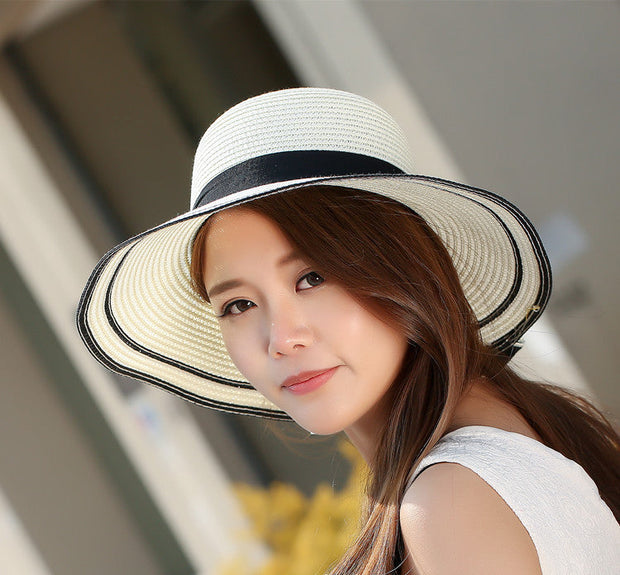 Woman wearing foldable straw sun hat with wide brim and black trim detail