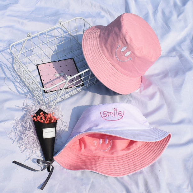 Pink and white cotton bucket fisherman hats with smiley face embroidery on light background