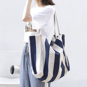 Woman carrying a high capacity striped canvas shoulder bag in navy and white for casual shopping or everyday use