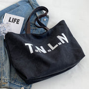 Black canvas letter printed tote bag with large capacity and shoulder straps, styled for college students and commuting.
