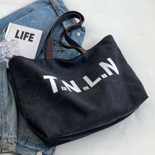 Black canvas letter printed tote bag with large capacity and shoulder straps, styled for college students and commuting.