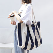 Woman carrying a large striped canvas shoulder bag in navy and beige while holding a cup