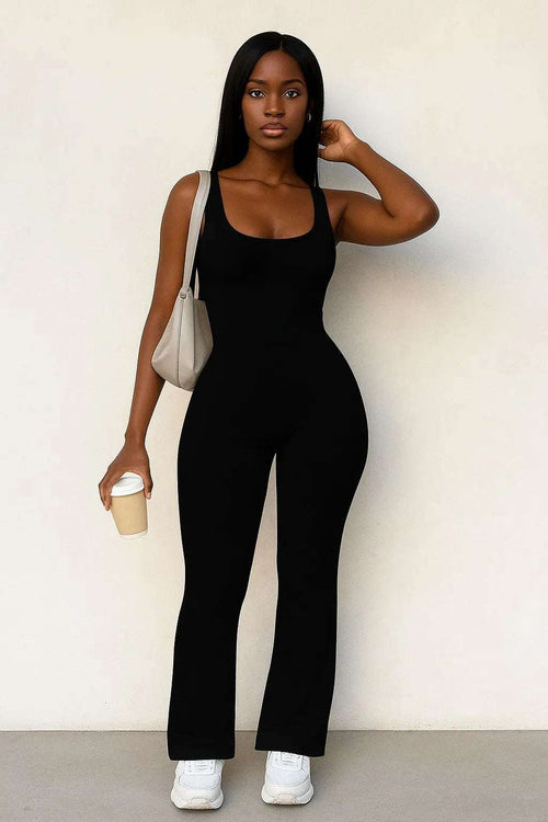 Woman wearing a sleek black Nova Night Out Jumpsuit holding a coffee cup and beige handbag against a plain background.